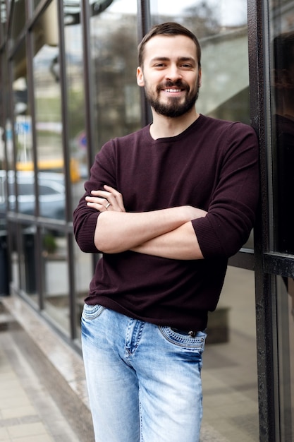 Stylish man with beard standing on the street in a leather coat. Photoshoot men on the street. A man in a fashionable style. Elegant men's hairstyle