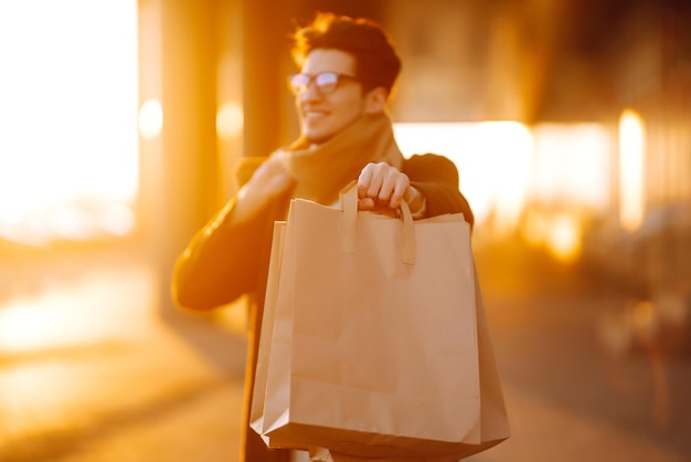 Stylish man with paper packages after shopping at sunset Handsome man doing shopping