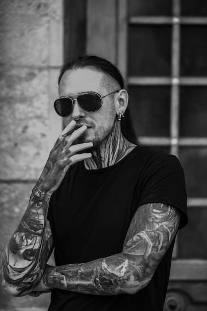 Foto uomo alla moda con i tatuaggi in occhiali da sole all'aperto