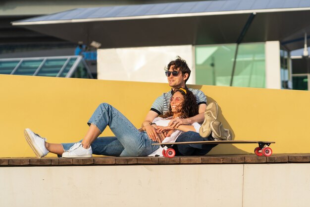 Stylish man and woman enjoy sunset cuddling at longboard\
relaxing after skateboarding in skate park