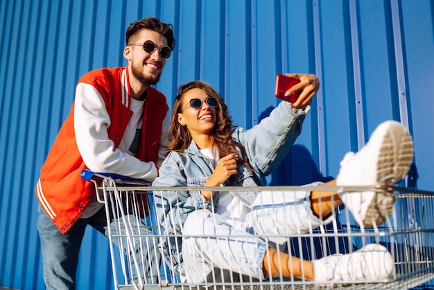 Stylish man and woman having fun and riding shopping cart Lifestyle leisure entertainment youth