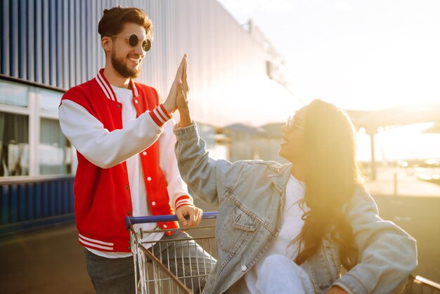Stylish man and woman having fun and riding shopping cart Lifestyle leisure youth concept