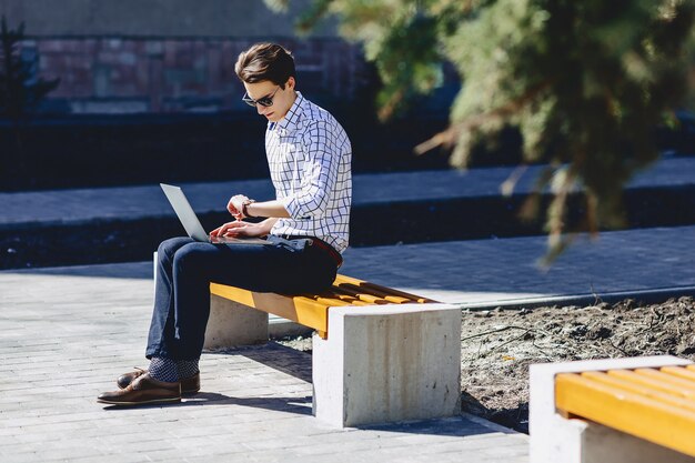 Стильный мужчина работает на ноутбуке на улице