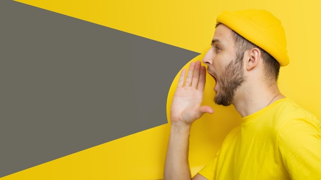 A stylish man on a yellow background shouts into an invisible megaphone. a place for your text or lo