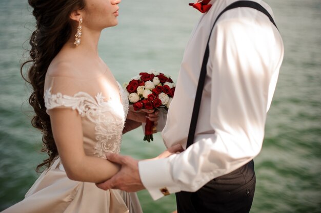 Stylish married couple with a wedding bouquet embracing in the background of the azure sea