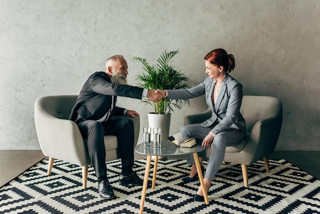 Stylish mature business partners shaking hands in loft interior