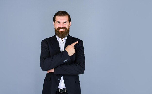 Stylish mature man pointing finger mens jacket wardrobe fashionable man dressed in suit formal fashion model handsome man standing on gray background happy bearded businessman copy space