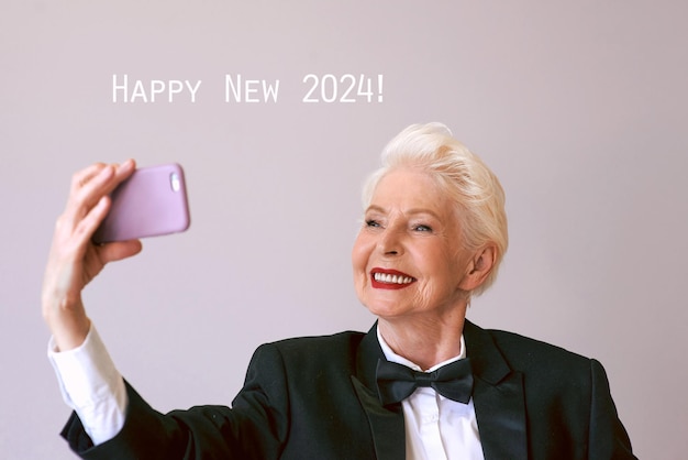 Photo stylish mature senior woman in tuxedo with cellphone video calling or making selfie fun party sty