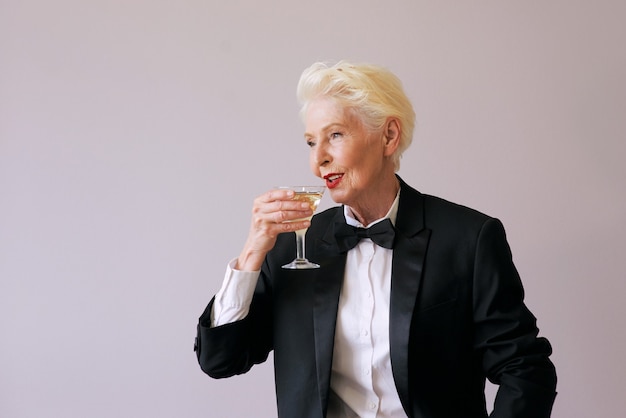 stylish mature sommelier senior woman in tuxedo with glass of sparkling wine