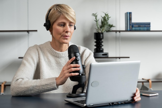 Photo stylish mature woman records an audio podcast in her cozy home apartment