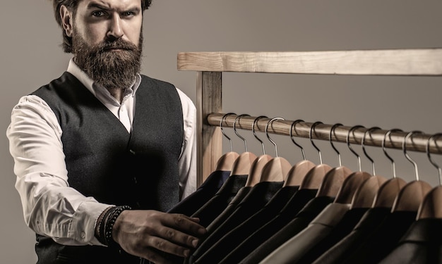 Stylish men's suit Handsome bearded fashion man in classical costume suit Man suit tailor in his workshop Male suits hanging in a row Tailor tailoring