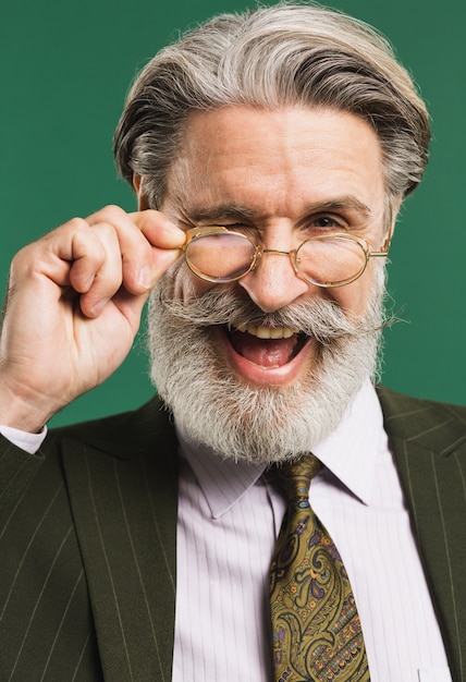 Stylish middle-aged bearded man in suit holding glasses over green wall