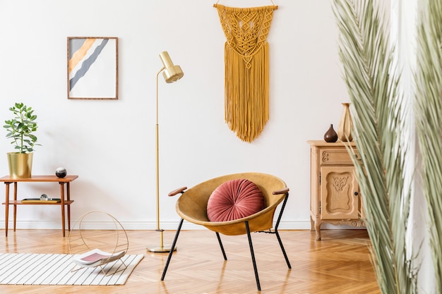 Stylish and minimalist interior of living room with design gold armchair, lamp, poster frames. dressing table with mirror, plants, yellow macrame and accessories in cozy home decor.