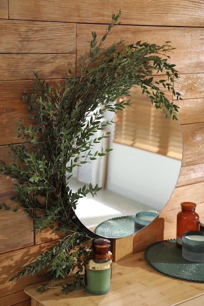 Стильное зеркало, украшенное зеленым эвкалиптом на деревянной стене в комнате