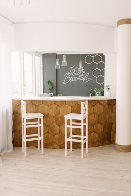 A stylish modern bar counter decorated with wooden tiles and\
two white bar stools in the living room of the house. scandinavian\
interior design