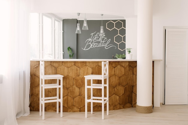 A stylish modern bar counter decorated with wooden tiles and two white bar stools in the living room