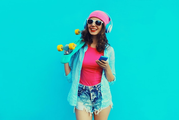 stylish modern happy young woman listening to music in headphones with smartphone skateboard