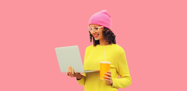 Stylish modern happy young woman working with laptop in colorful clothes on pink studio background