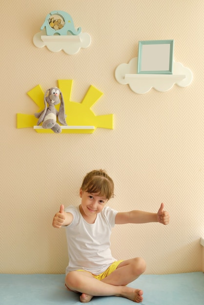 세련되고 현대적인 인테리어 디자인. 아이 방을 위한 집. 아이는 새로워진 방에서 기뻐합니다. 사진 프레임이 있는 일반 베이지색 벽에 흰 구름 형태의 어린이 선반.