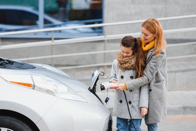 Madre e figlia alla moda caricano un'auto elettrica e trascorrono del tempo insieme