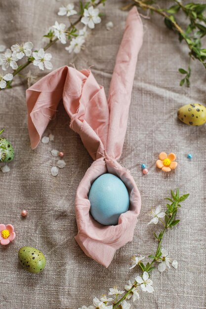 Stylish natural dyed easter egg in bunny ears napkin with spring flowers on rustic table Happy Easter Modern easter table setting Rustic Easter still life