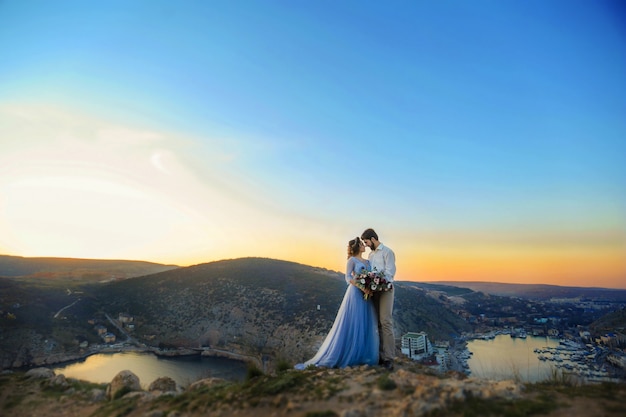 A Stylish newlyweds cuddle in nature, on the background of rocks and cliffs.