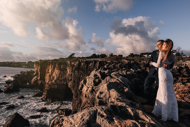 Stylish newlyweds on the high and rocky shore of the ocean sky