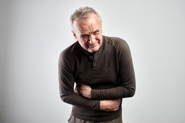 Stylish old man clutching his abdomen isolated on white, feels discomfort in intestines and stomach, writhing in pain