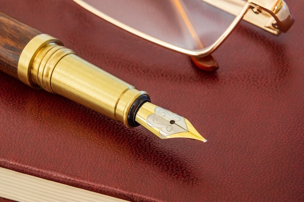 Stylish pen with a gold plated pen and glasses on brown notepad