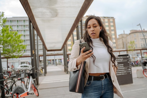 Stylish pensive mixed race woman using mobile phone reading text message, shopping online