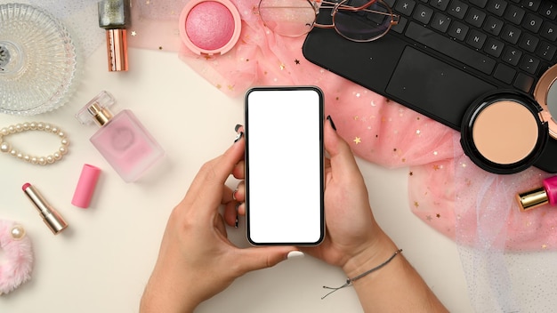 Stylish pink feminine beauty blogger workspace with hands holding a smartphone top view flat lay