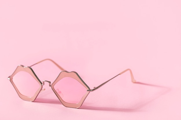 Stylish pink sunglasses in shape of lips on pink background with shadow and copy space