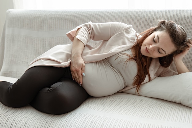 Стильная беременная женщина в последний месяц отдыхает на диване у себя дома.