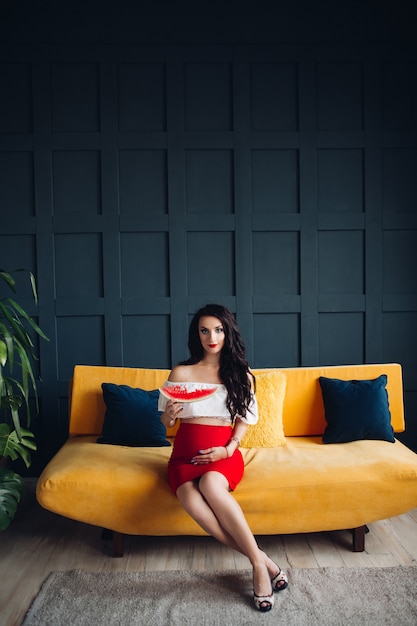 Stylish pregnant woman sitting on orange sofa and posing