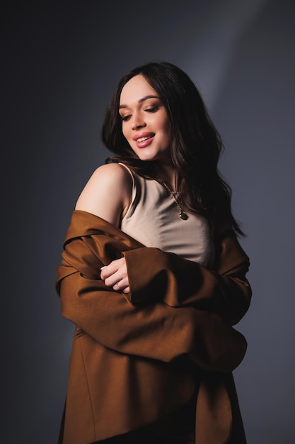 Stylish pretty young woman in brown classic suit sitting on gray background Beautiful woman in a jacket and with makeup on her face