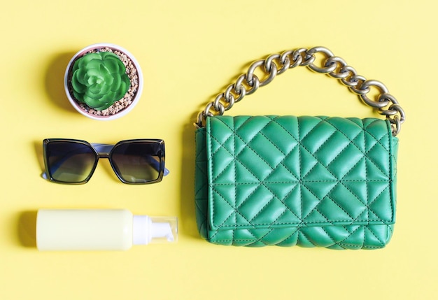 Stylish quilted green handbag sunglasses cream and a flower on a yellow background