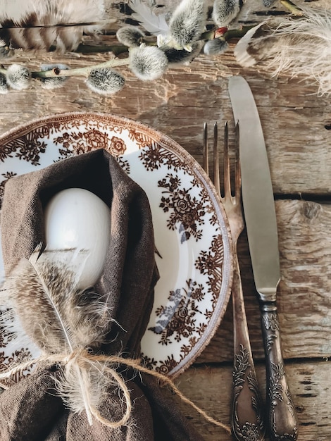 Stylish rustic easter table setting natural egg napkin feathers\
plate cutlery on aged wood