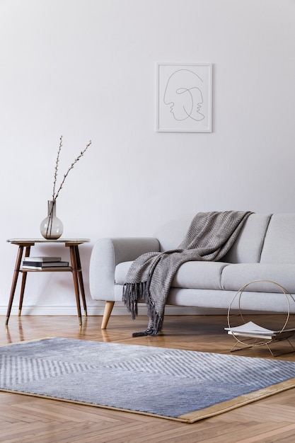 Photo stylish scandi interior of home space with design grey sofa, retro wooden table, mock up poster frame, decoration , carpet and personal accessories in elegant home decor.