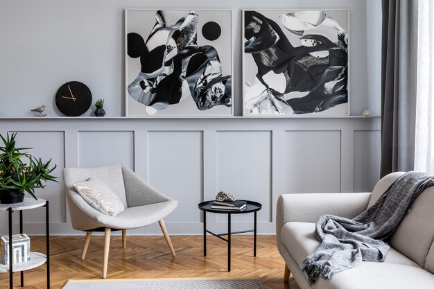 Elegante interno della casa scandinava del soggiorno con divano grigio di design, poltrona, sgabello in marmo, tavolino da caffè nero, dipinti moderni, decorazioni, piante ed eleganti accessori personali nell'arredamento della casa.