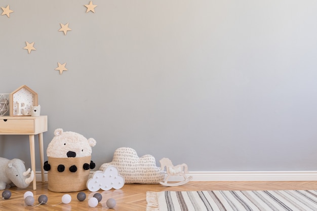 Stylish scandinavian kid room with copy space, toys, teddy bear, plush animal and children accessories. Modern interior with grey background walls. Template. Design home staging.