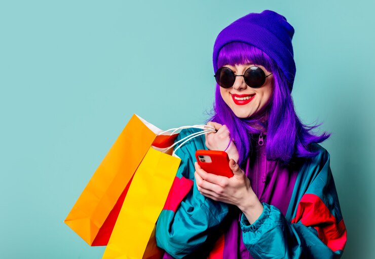 Photo stylish shopaholic girl in  tracksuit and sunglasses hold shopping bags and mobile phone on blue wall