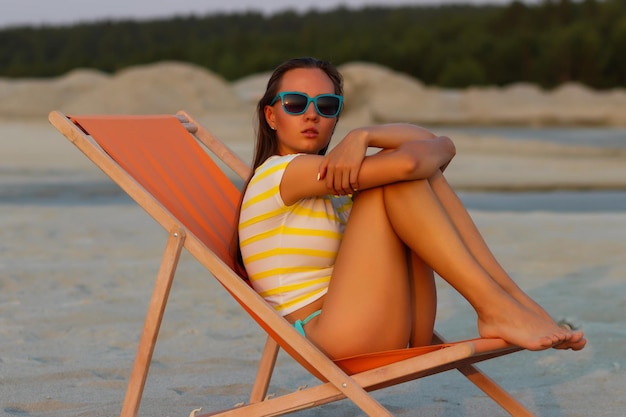 Stylish slim woman in deckchair on shore