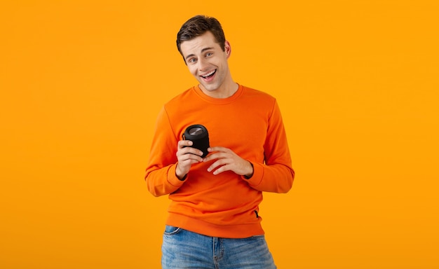 Stylish smiling young man in orange sweater holding wireless speaker happy listening to music having fun on orange