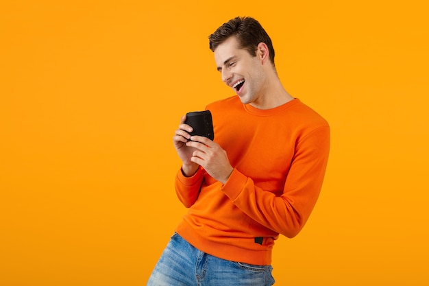 Stylish smiling young man in orange sweater holding wireless speaker happy listening to music having fun