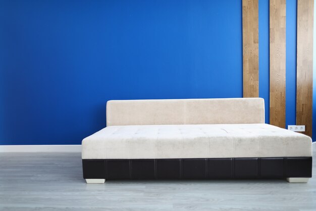 Stylish sofa stand on floor in room against blue wall.