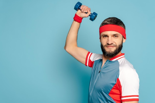 Stylish sportsman exercising with dumbbell on blue background