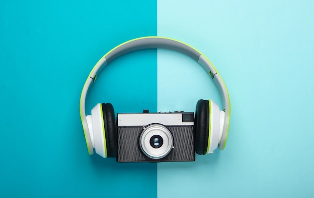 Stylish stereo headphones with retro camera on blue surface