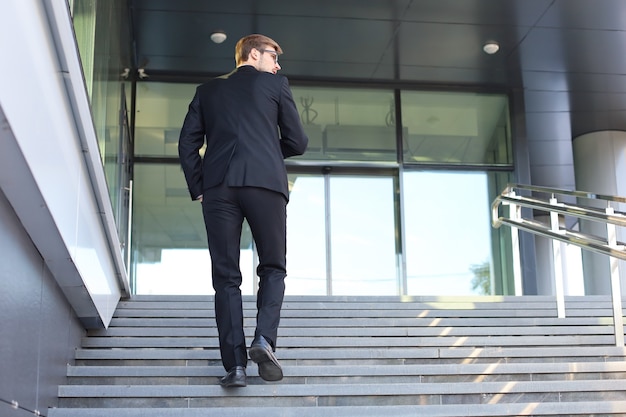 Stylish successful businessman goes up the stairs of the office building.