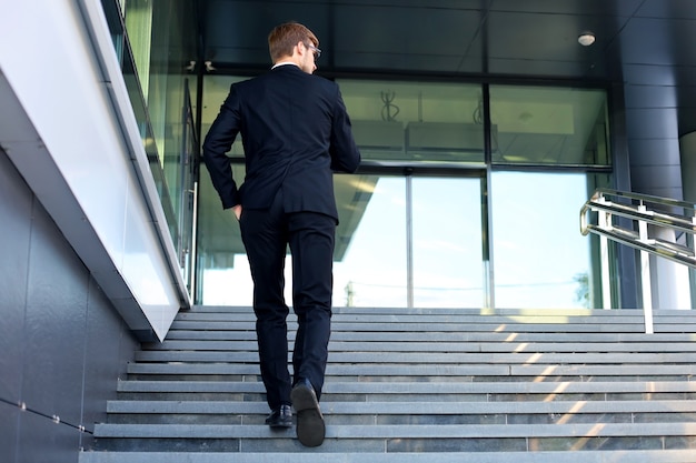 Foto elegante uomo d'affari di successo sale le scale dell'edificio per uffici.