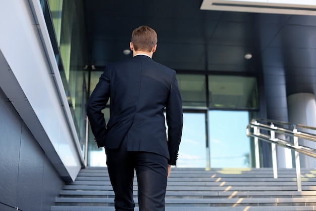 Photo stylish successful businessman goes up the stairs of the office building.